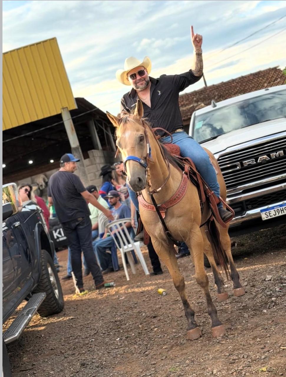 Jeff da RAM a cavalo, com o dedo erguido, ao lado de uma RAM branca durante um evento country